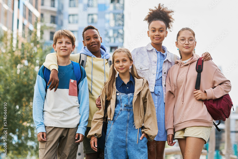 Group of five multicultural secondary school learners in casualwear standing in row in urban environment and looking at camera