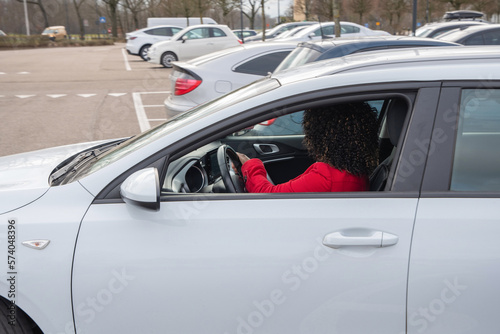 African american woman in red coat driving with a white car out of the parking