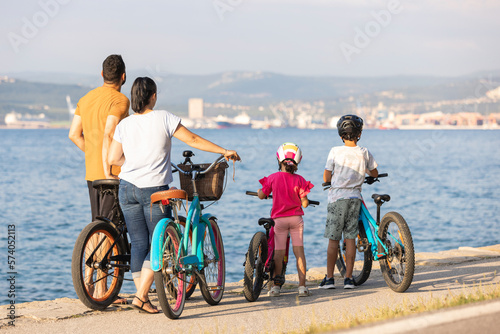 Caucasian family with two children standing on bicycles and enjoying the sunset on a seashore, rear view.