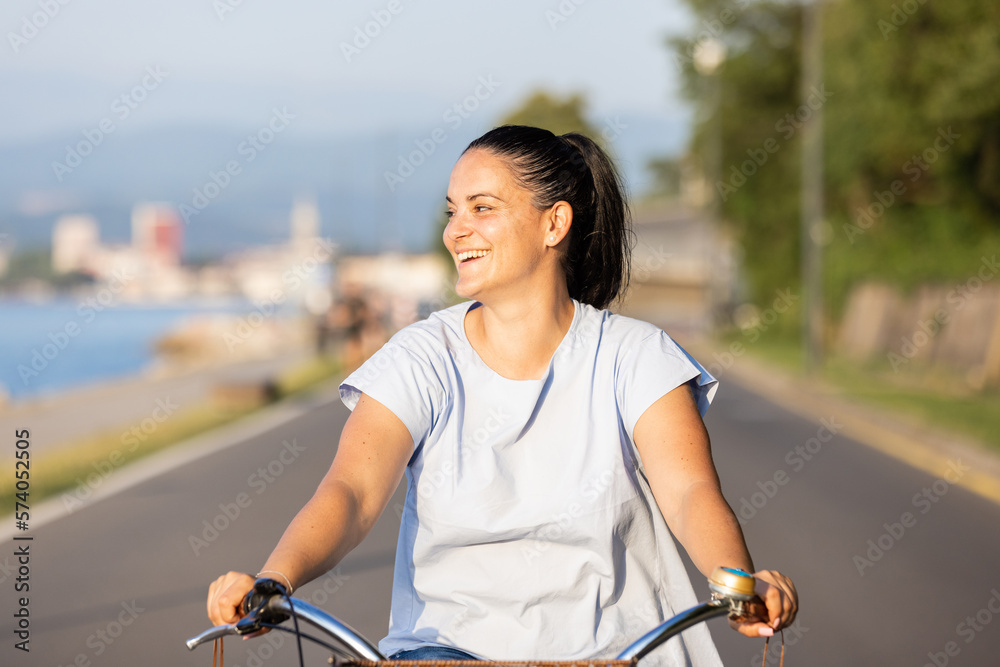 Happy smiling woman riding bicycle along the coast at summer