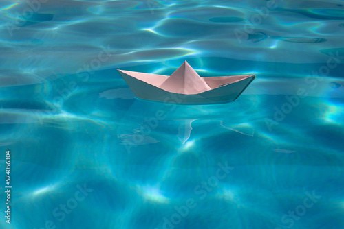 Sailing yacht concept, paper ship with sailing boat. Paper boat on the sea background. Origami paper boat sailing on water causing waves and ripples.