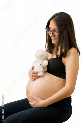 Expecting Comfort: Pregnant Woman Sitting with Stuffed Animal in White Studio Background