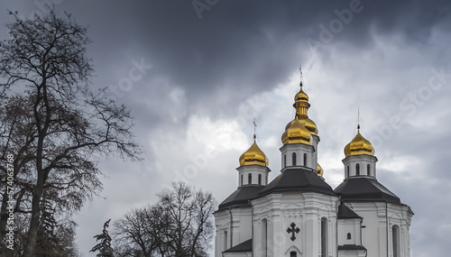 An Orthodox church with white facades and golden domes against a cloudy cloudy sky and clouds, on a cloudy spring day