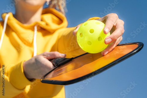 Pickleball paddle and yellow ball close up, woman playing pickleball game, hitting pickleball yellow ball with paddle, outdoor sport leisure activity