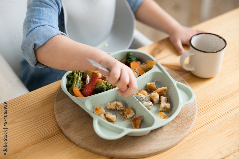 Top view of how a toddler boy pricking food with a fork from a special children's plate. Concept of self-feeding. BLW. Child without the help of adults eats healthy vegetables with meat. close-up Top view of how a toddler boy pricking food with a fork from a special children's plate. Concept of self-feeding. BLW. Child without the help of adults eats healthy vegetables with meat. close-up
