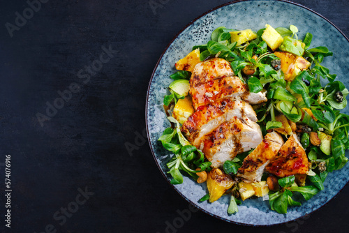 Traditionaler deutscher Feldsalat mit Hähnchen Brust, Obst und Cashewnüsse serviert mit würziger süß sauer Sauce als Draufsicht auf einem Nordic Design Teller mit Textfreiraum links