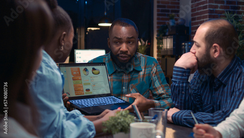 Diverse coworkers brainstorming, african american employee showing data charts on laptop screen. People planning strategy in business meeting, discussing presentation, team communication