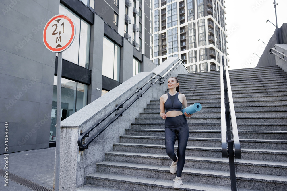 Smiling woman in activewear coming down stepway for exercising outdoors.