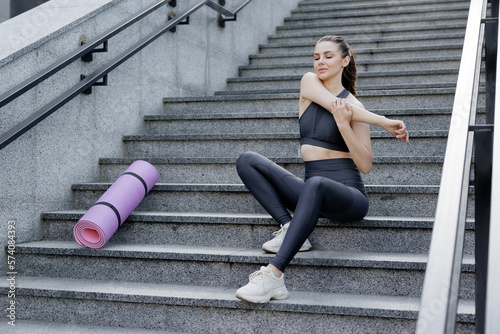 Focused female athlete warming up on stairway in city.