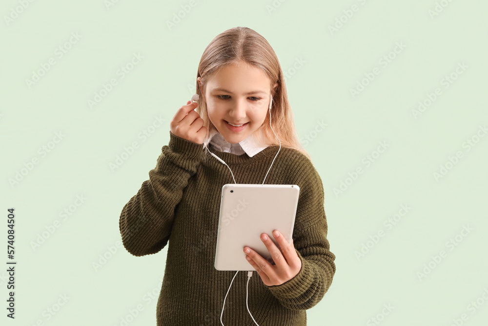 Little girl with tablet computer putting earphones on green background Little girl with tablet computer putting earphones on green background