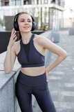 Beautiful sportswoman with headphones posing, after morning workout outside.