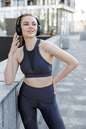Beautiful sportswoman with headphones posing, after morning workout outside. © Tymoshchuk