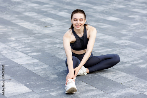 Smiling sporty lady with dark hair exercising, stretching body on street.