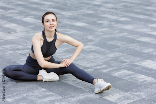 Motivated sporty girl stretching legs during warm-up at urban area.