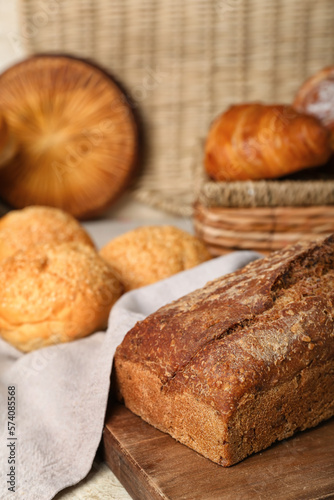 Cutting board with loaf of rye bread and delicious buns on napkin, closeup