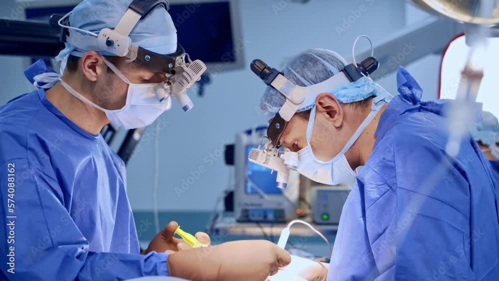 Two surgeons cooperate at operation in modern surgery room. Focused doctors use the instruments at procedure. Two surgeons cooperate at operation in modern surgery room. Focused doctors use the instruments at procedure.