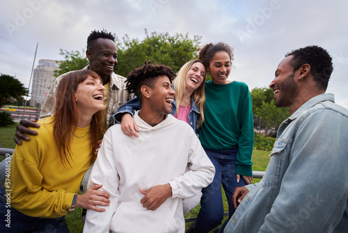 Young group of cheerful multiracial friends looking at each other and laughing outdoors. Concept of tourism, travel, leisure and adolescence. People spending time together in the city park. #574088539