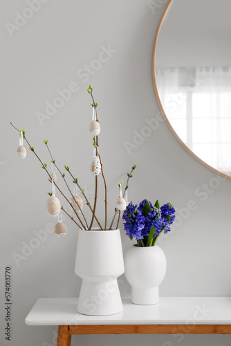 Vases with tree branches  Easter eggs and flowers on table in room