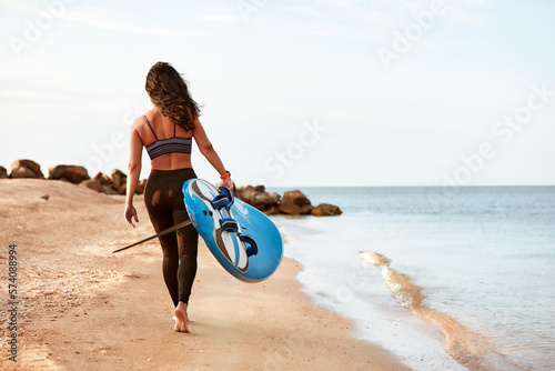 Woman surfer with surfboard going to surf at seaside. Girl holding surfboard o and goes to the ocean sea, a view from the back