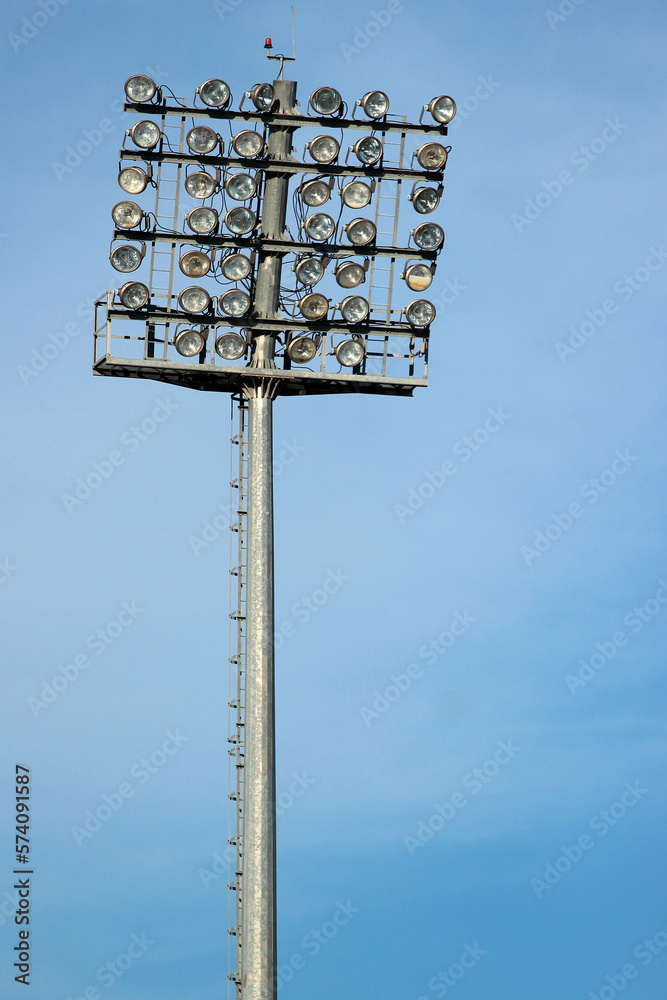 Tall lamp post, stadium light or sports lighting against blue sky background Tall lamp post, stadium light or sports lighting against blue sky background