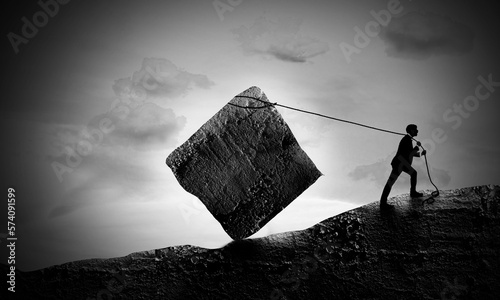 Fotografia Surreal scene Of Young Businessman Pulling A Rock Block up to Hill