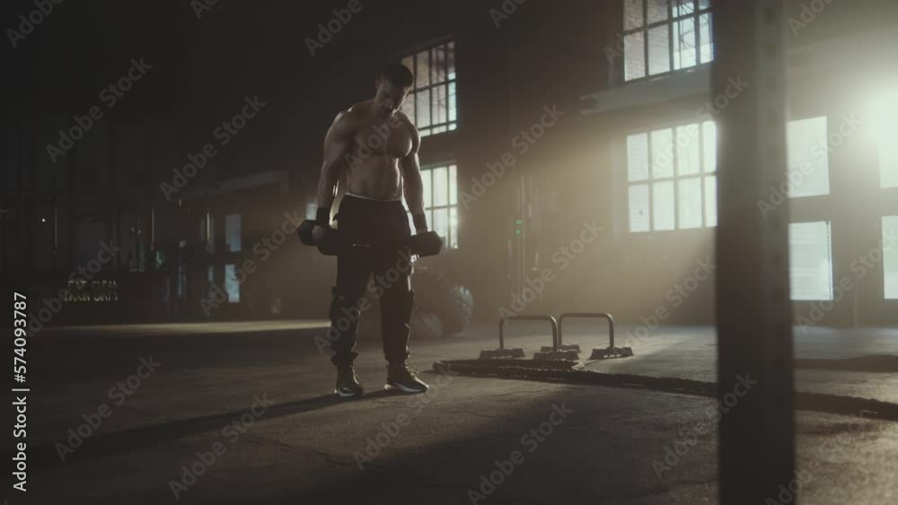 Full shot of a strong athletic sweaty man doing shirtless workout at gym, training with dumbbells in slow-motion Full shot of a strong athletic sweaty man doing shirtless workout at gym, training with dumbbells in slow-motion