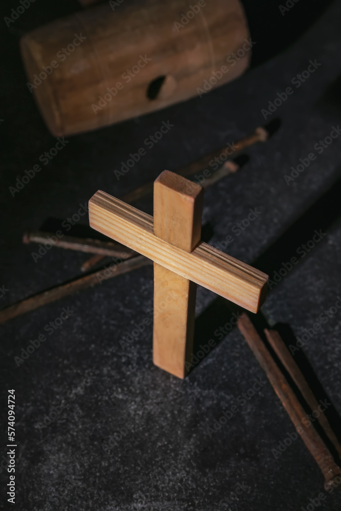 Wooden cross with nails and mallet on dark background, closeup. Good Friday concept