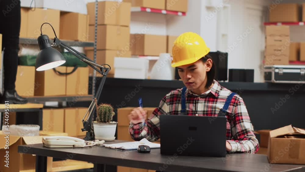 Warehouse employee looking at stock logistics on pc, checking quality of products before planning shipment. Young man working on merchandise products, using laptop for inventory. Handheld shot. Warehouse employee looking at stock logistics on pc, checking quality of products before planning shipment. Young man working on merchandise products, using laptop for inventory. Handheld shot.