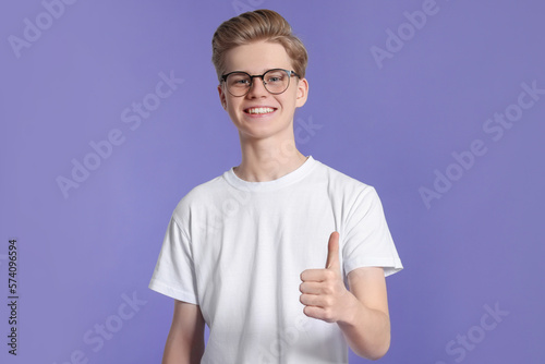 Teenage boy showing thumb up on purple background