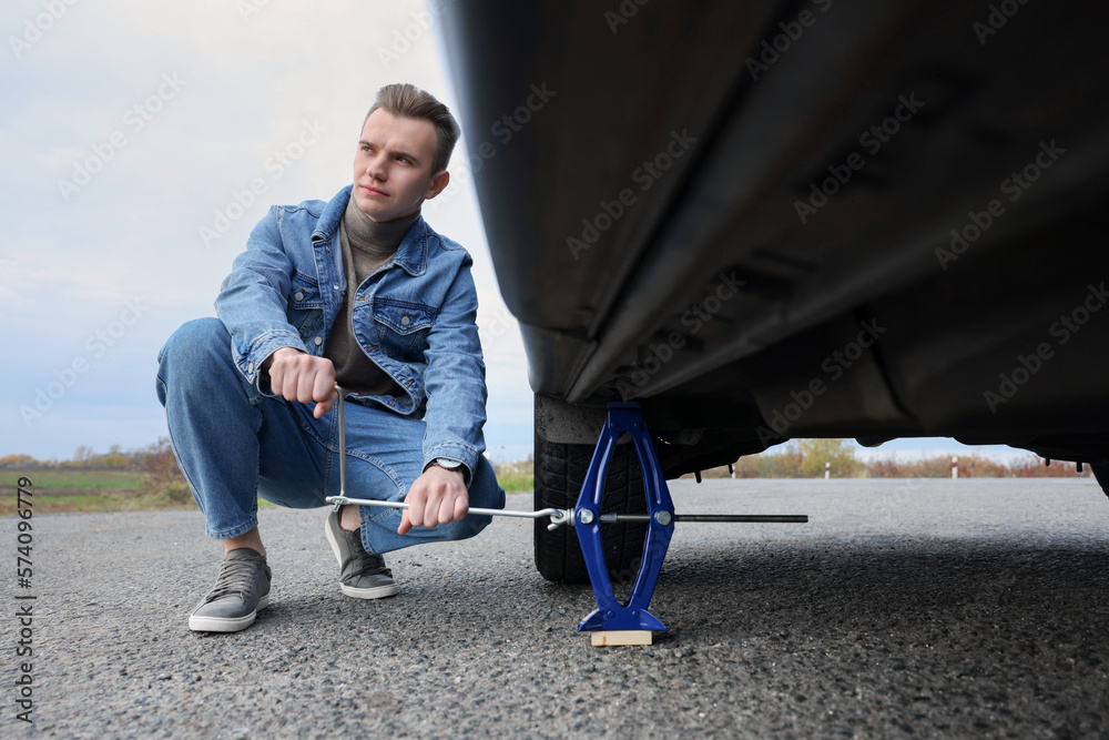 Young man changing tire of car on roadside