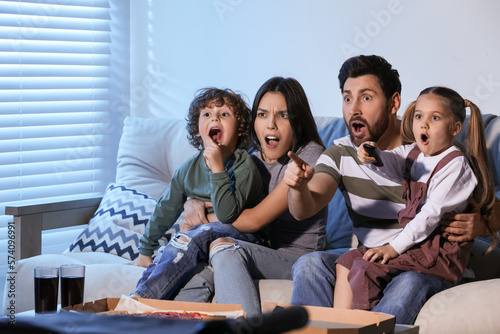 Surprised family watching TV with pizza on sofa at home