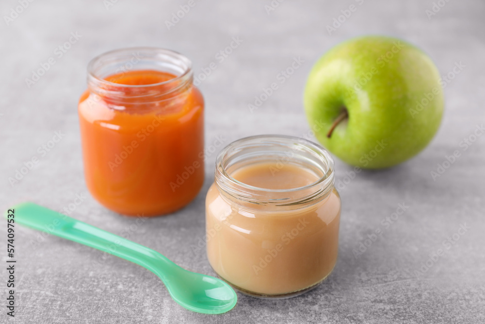Jars with healthy baby food, apple and spoon on light grey table Jars with healthy baby food, apple and spoon on light grey table