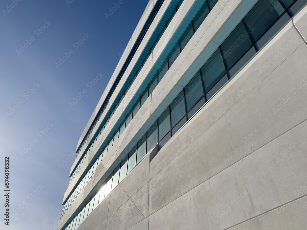 The exterior wall of a contemporary commercial style building with concrete prefabricated panels and glass windows. The futuristic building has engineered cement cladding frame panels. The exterior wall of a contemporary commercial style building with concrete prefabricated panels and glass windows. The futuristic building has engineered cement cladding frame panels.