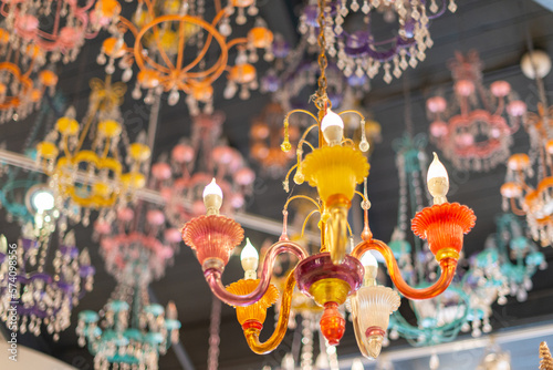Multiple antique colorful orange and yellow glass blown and hand painted decorative chandeliers with illuminated electric lightbulbs. The crystal lights are hanging from the ceiling glowing prisms. 
