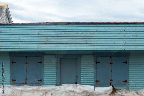 Wallpaper Mural A blue color exterior wooden wall of a vintage warehouse or garage with multiple double doors and a single wooden door in the middle. The wooden doors are a darker shade of blue. It's winter with snow Torontodigital.ca