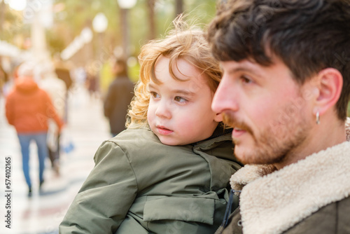 A blond preschooler in the arms of his young father in a park.