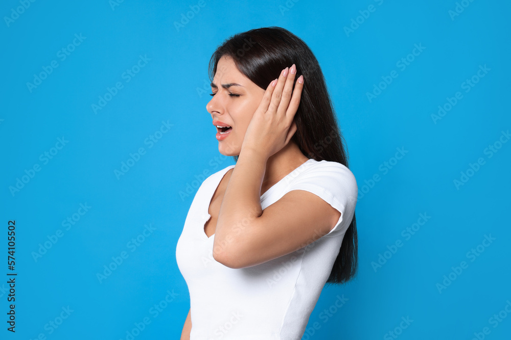 Young woman suffering from ear pain on light blue background Young woman suffering from ear pain on light blue background