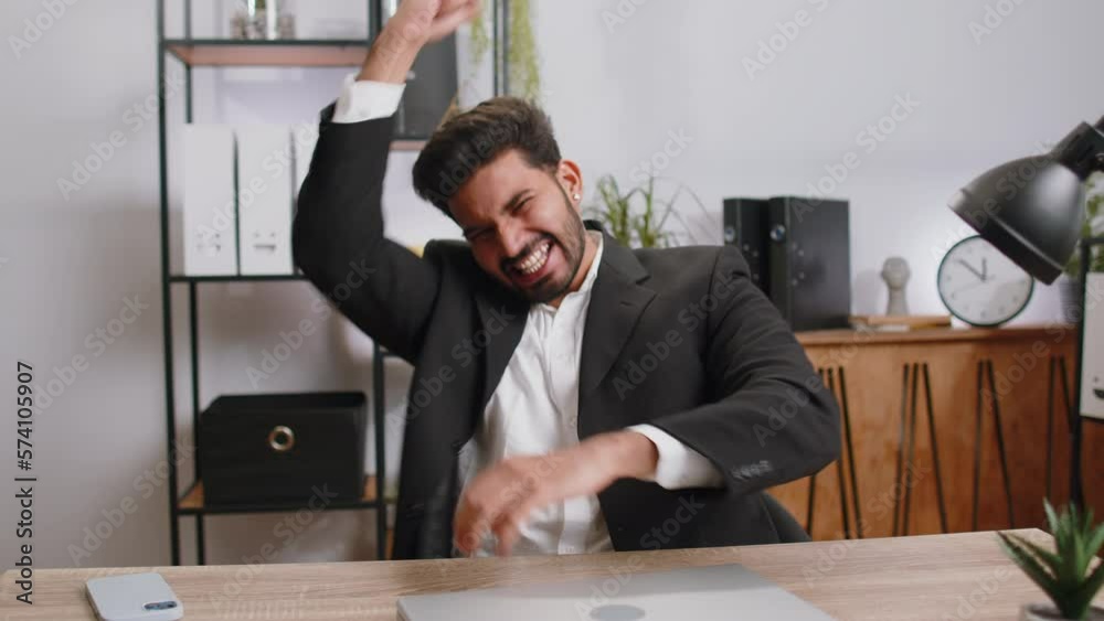 Happy amazed young indian businessman working on laptop shocked by sudden victory, game winning, lottery goal achievemen, good career news. Excited manager man freelancer at home office workplace desk