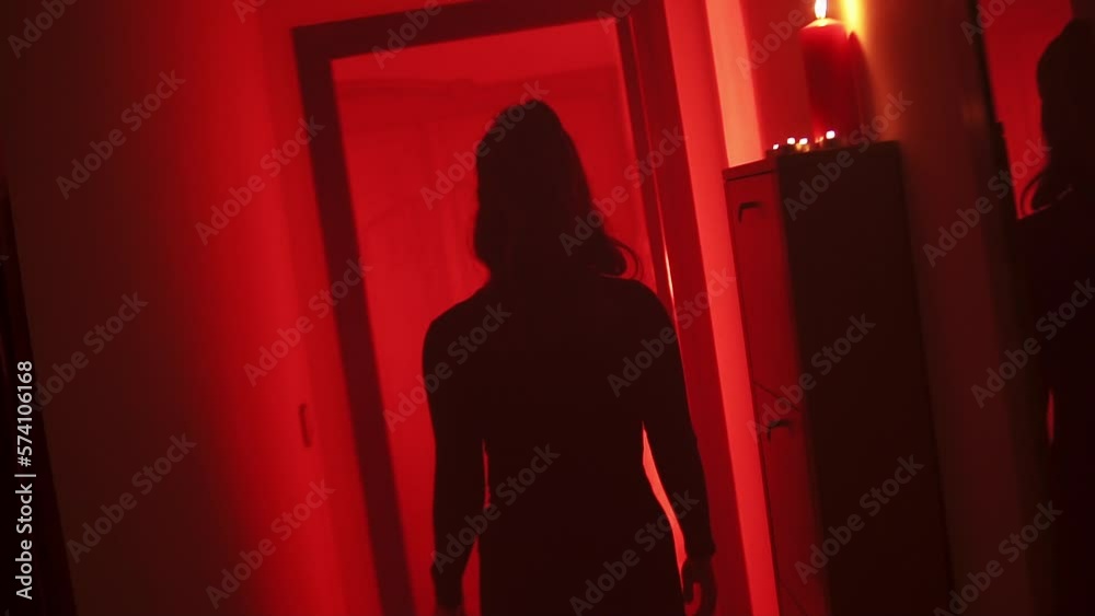 Black silhouette of a curvy woman walking with her back to the camera in a corridor with a red low light environment.
