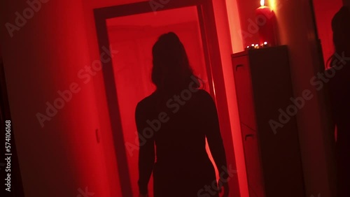 Black silhouette of a curvy woman walking with her back to the camera in a corridor with a red low light environment.