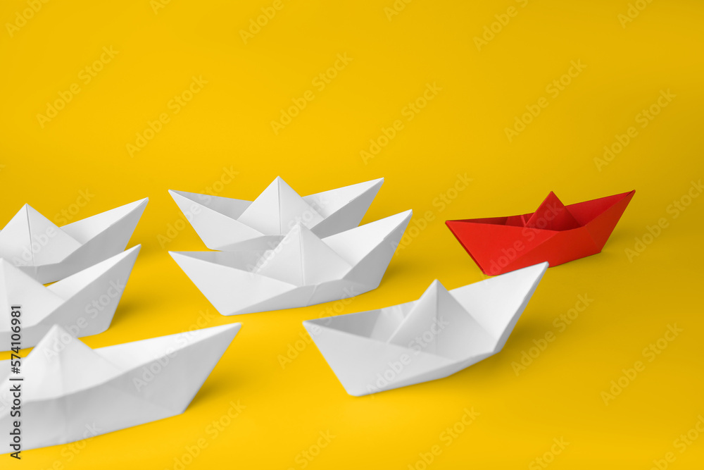 Obraz premium Group of paper boats following red one on yellow background. Leadership concept