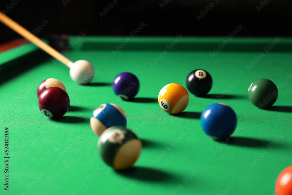 Many colorful billiard balls and cue on green table indoors Many colorful billiard balls and cue on green table indoors