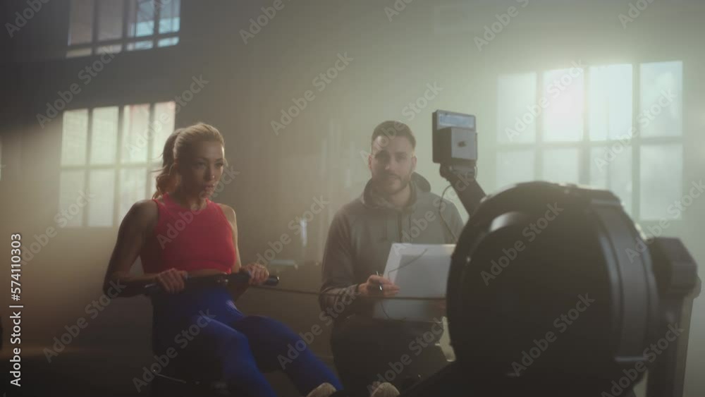 Young woman working out on the rowing machine, personal trainer explaining the technique and writing down the speed in paper Young woman working out on the rowing machine, personal trainer explaining the technique and writing down the speed in paper