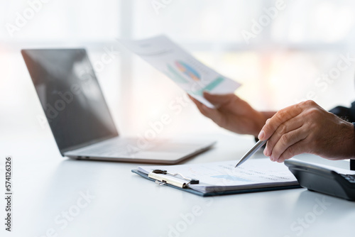 Young Asian businessman examining chart analyzing documents Financial data graph showing investment income in real estate business in office accounting management concept.