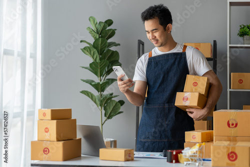 Entrepreneur, small business, SME, young freelance Asian man working from home with lots of boxes on the side. Use smartphones and laptops for commercial auditing, marketing, packaging, online sales.