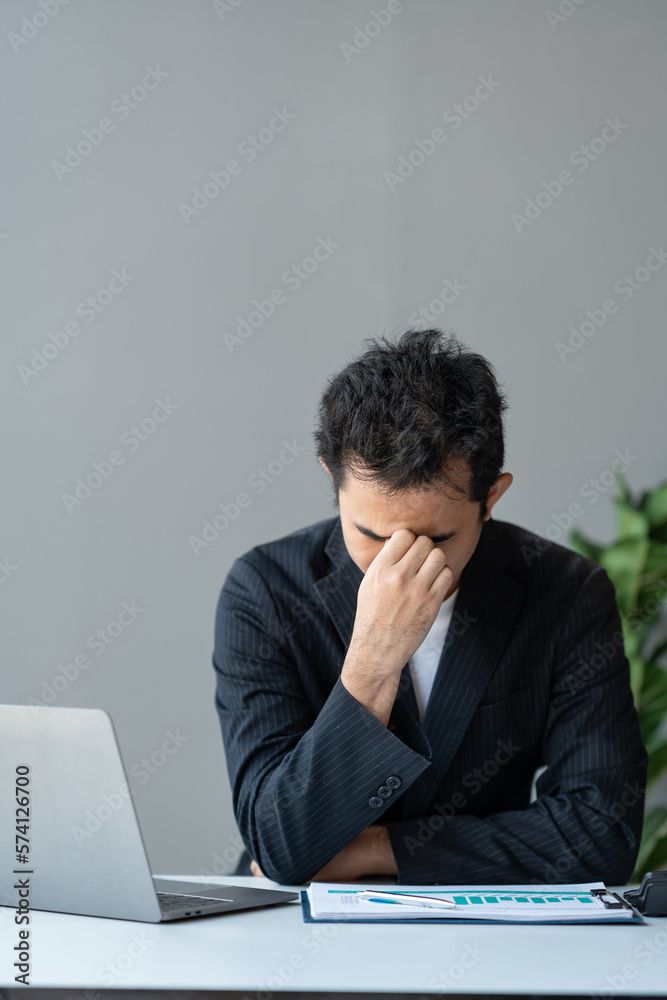 Young asian businessman suffering from stress, eyestrain, headache searching for financial information, stats, graphs, income charts. while working online on laptop computer at office. Young asian businessman suffering from stress, eyestrain, headache searching for financial information, stats, graphs, income charts. while working online on laptop computer at office.