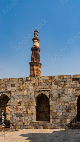 The ancient temple complex of Qutub Minar. Weathered sandstone brick walls with arches. The world's tallest minaret against the blue sky. India. Delhi.