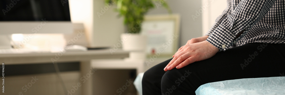 Closeup of young woman sitting on couch with folded hands on knees