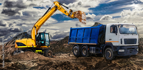 An orange wheeled excavator is loading a dump truck at a construction site. Loading a vehicle for transporting soil. Excavator moves the soil. equipment for earthworks.