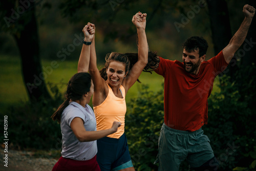 Group of runners running marathon outdoors. They are running in the mountains at sunset. Wearing sports clothes. Smiling. Running through the finish with arms raised.